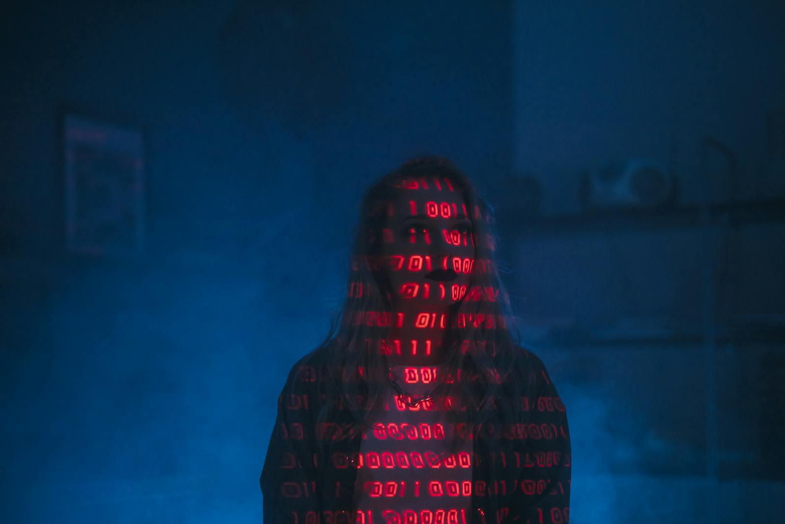 A mysterious silhouette with red binary code projected over the face, set against a dark, moody background.